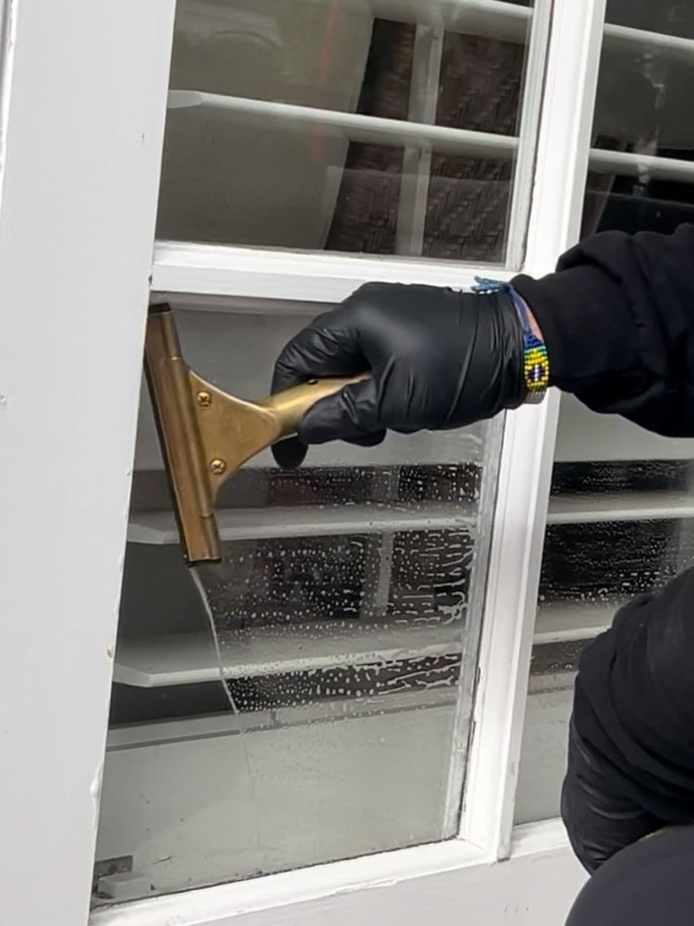 Person using a squeegee to clean a glass window, wearing black gloves.