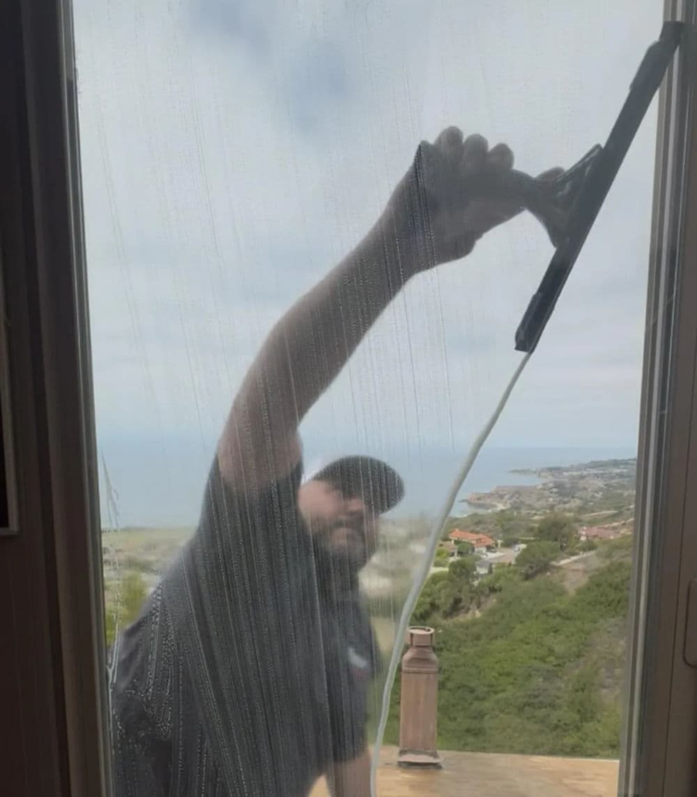 Window cleaner using a squeegee to clean glass with a scenic coastal view in the background.